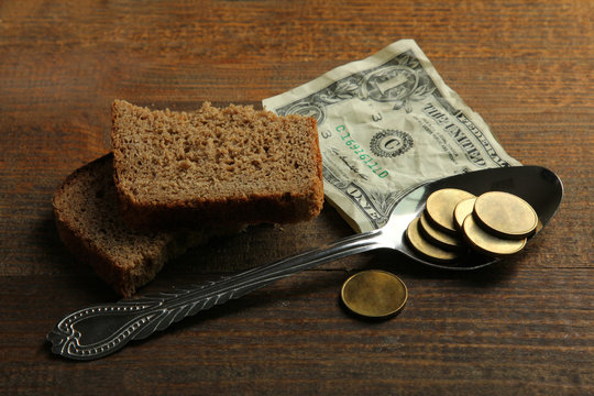 a penny and a crumpled dollar with bread slices and an iron spoon on brown wooden background.The concept of poverty
