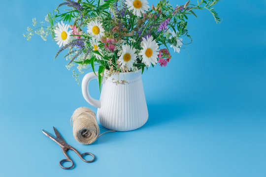 bouquet of wildflowers in jar on plain blue background