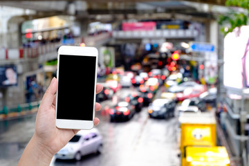 Hand with Smart phone with blank screen and abstract blur bokeh of traffic jam on road in the city on the background