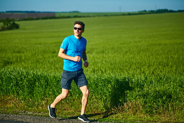 man runner athlete jogging along a green field in the early morning. man fitness sunset jogging workout wellness concept. free space in front of the person