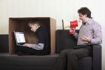 Tween son sitting in a cardboard box with a laptop while his father yells at him through a megaphone