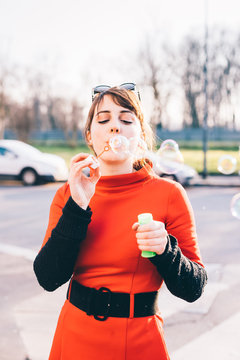 young beautiful red dressed vintage hipster woman in street town playing with bubble soap - childhood, having fun, happiness concept