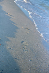 Fototapeta na wymiar Footprints on the wet sand, waves at sunset on a quiet beach. Ti