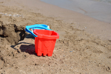 Fototapeta na wymiar Red bucket on the wet sand on the beach in a summer sunny day. C