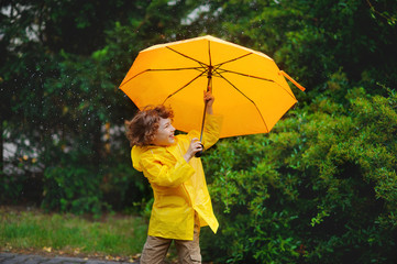 Boy of 8-9 years stand in the rain with a big yellow umbrella.