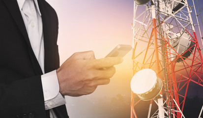 Businessman using mobile phone, with satellite dish telecom network on telecommunication tower at sunrise in rural city