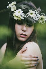 Outdoor portrait of beautiful young woman in a white dress wearing floral wreath.