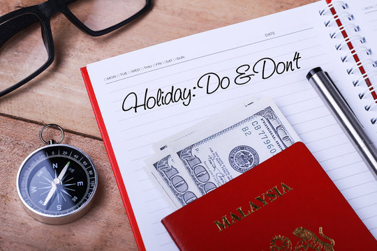 Holiday: Do & Don’t text message on note book with passport, glasses, hundred dollar bills, compass and pen on wooden table. - Powered by Adobe