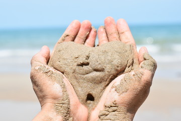 two hands holding sand in the shape of a heart