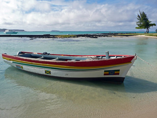 Fototapeta premium Cap Malheureux, village au nord de l'île Maurice, océan Indien. Un bateau coloré en bois est amarré dans une eau claire et transparente. Au second plan, eau turquoise, ciel bleu et nuages blancs
