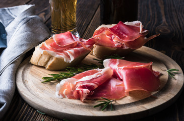 Spanish tapas with jamon, glass and bottle of beer on a wooden background