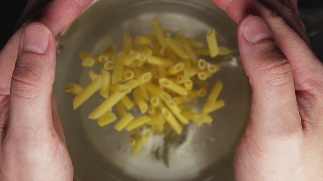 SLOW MOTION: A chief-cooker's hands throw a pasta in a steel pan (top view)