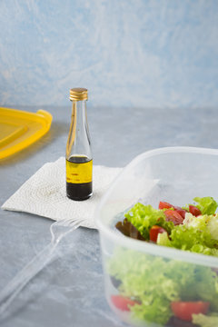 Prepared at home takeaway container with fresh lettuce and cherry tomatoes salad and small bottle with mix of olive oil and balsamic vinegar. Selective focus.