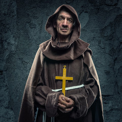 Monk holding a wooden cross in front of the old walls - 114049014