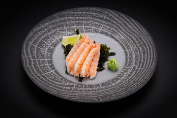 Japanese cuisine. Sushi. Shrimp sashimi on a round plate with lime and wasabi