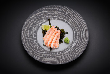 Japanese cuisine. Sushi. Shrimp sashimi on a round plate with lime and wasabi