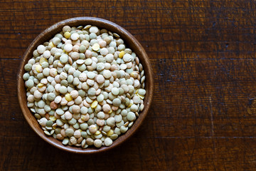 Rustic bowl of green uncooked lentils isolated on dark wood from