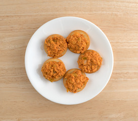 Spicy chicken salad on butter crackers on a white plate top view on a wood table top.