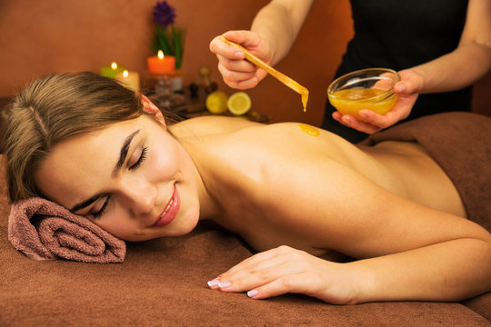 Beautiful woman in spa salon having spa therapy honey procedure with hands of masseur