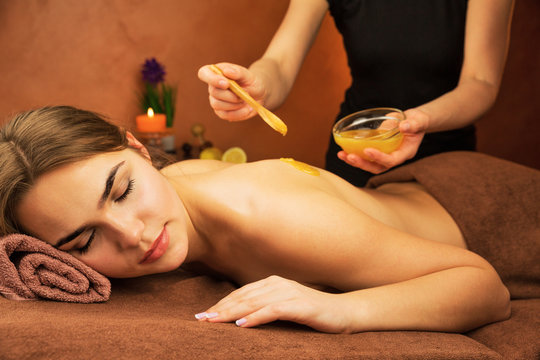 Beautiful woman in spa salon having spa therapy honey procedure with hands of masseur