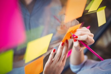 Businesswoman writing on sticky notes stuck to glass