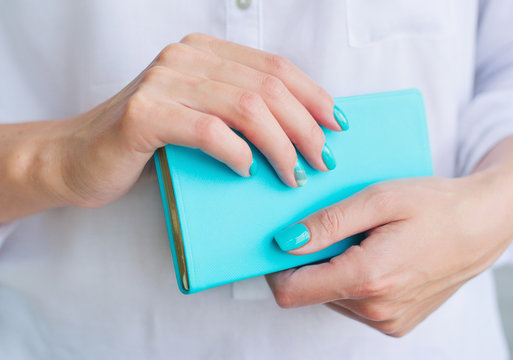 Closeup woman hands with elegant turquoise manicure holding blue diary