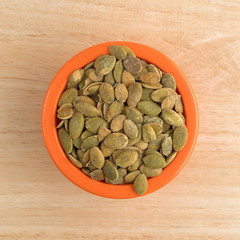 Organic dry roasted pumpkin seeds in a small orange bowl on top of a wood table.