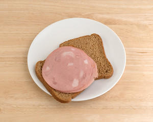 Mortadella sandwich on wheat bread white plate atop a wood table top. © Bert Folsom