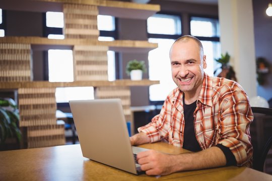 Happy businessman using laptop at desk in creative office