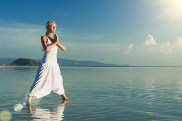 Fototapeta na wymiar Young woman doing yoga at sunset. Girl doing balance practice at the beach. Lens flare effect
