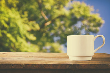 Cup of coffee a wooden table in front of tress background