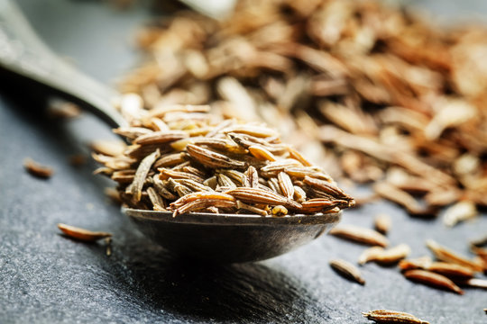 Zira or cumin in a metal spoon on a dark background, close-up, s