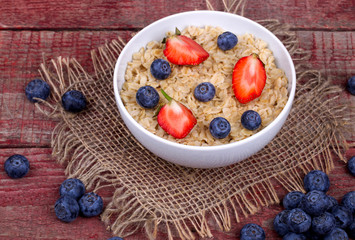 Breakfast with porridge, strawberry and blueberry on a wooden ta