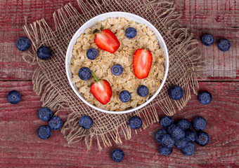 Breakfast with porridge, strawberry and blueberry on a wooden ta