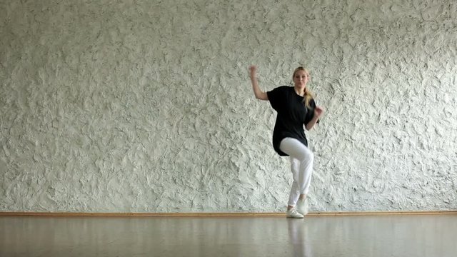 Young hip-hop and house female dancer performing against a light wall in the dancing hall
