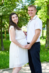 pregnant woman with husband posing in the city park, family portrait, summer season, green grass and trees
