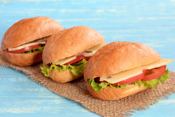 Sandwiches with sliced cheese, fresh tomato and lettuce. Useful sandwiches on burlap and blue wooden background. Vegetarian lunch recipe. Healthy food idea. Closeup