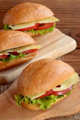 Sandwiches with cheese, fresh tomato and lettuce. Vegetarian sandwiches on a cutting board and a brown wooden background. Healthy breakfast, lunch. Picnic food idea
