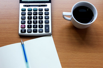 Notebook with pen, calculator and white cup of coffee