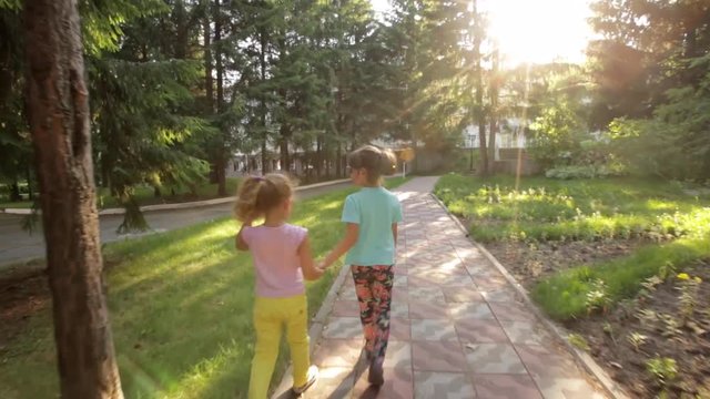 two little girls walk through the Park and holding hands. children spend time outdoors