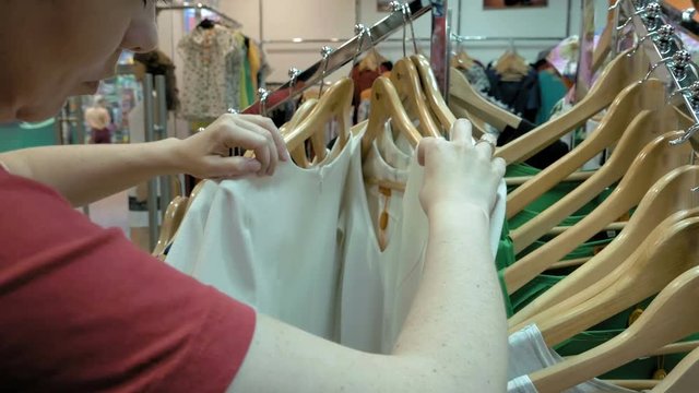 A female customer is browsing through the cloths. Video shows a female contemplating in which shirt to pick. Variety of sizes and color are offered. 4K UHD video footage.