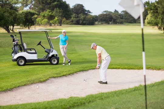 Golfer playing on sand trap by woman