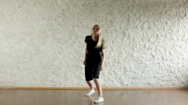 Young hip-hop and house female dancer dressed in black performing against a light wall in the dancing hall