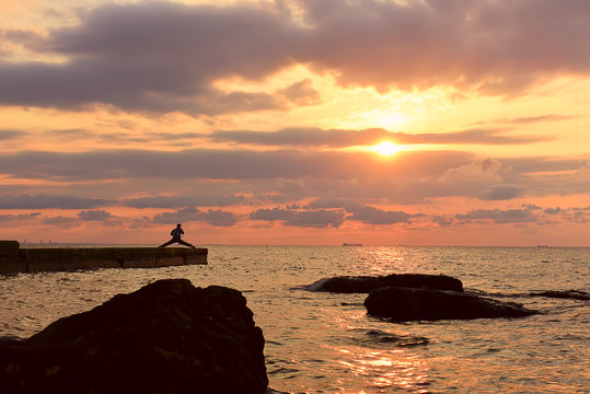 beautiful beautiful sunrise over the sea. Beautiful sky with beautiful clouds. Silhouette of man on the pier in for sports, yoga at dawn. Sun rays through the clouds at dawn
