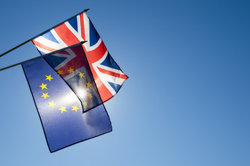 European Union and British Union Jack flag flying together in front of bright blue sky in...