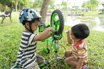 Happy family of two brothers little boys repairing bicycle wheel, outdoors.
