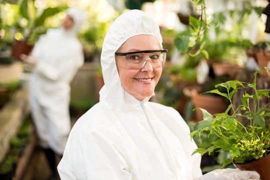 Female Scientist In Clean Suit Holding Potted Plant 