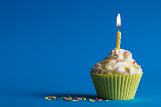 yellow birthday cupcake with burning candle and blue background