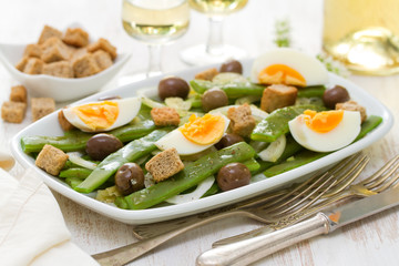 salad green beans with olives and croutins on white dish and glass of white wine