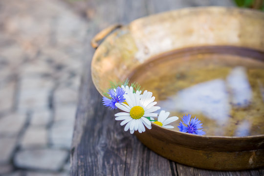 Daisies and cornflowers in a copper basin of water on the background of a wooden surface